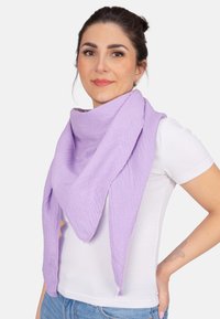 Écharpe triangulaire violette en tissu doux et texturé avec un aspect froissé, portée par-dessus une chemise blanche sur un fond neutre.