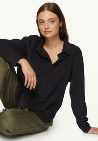 Schwarzes Langarmhemd mit Button-Down-Kragen, lockere Passform und strukturiertem Stoff, kombiniert mit olivgrünen Hosen.