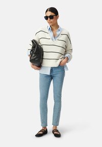 Sweter w kremowe paski nałożony na jasnoniebieską koszulę z kołnierzykiem, w połączeniu z jasnoniebieskimi dżinsami z wyszywanymi akcentami i czarnymi płaskimi butami.