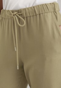 Ljust olivgröna joggers med en slät textur, elastisk midja och justerbar dragsnöre. Har sidofickor för extra bekvämlighet.