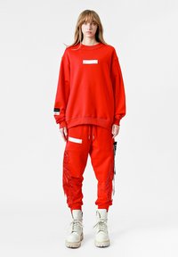 Sudadera roja y pantalones de chándal a juego, fabricados en una mezcla de algodón, con rayas laterales, acentos reflectantes y detalles de flecos en los pantalones.
