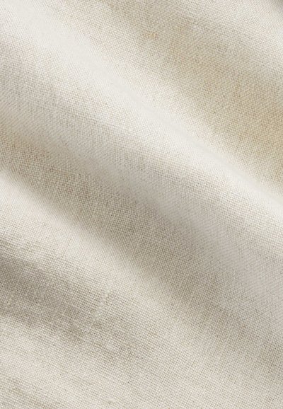 Gros plan sur un tissu tissé beige clair lisse avec une texture fine et de doux plis créant des ombres douces.