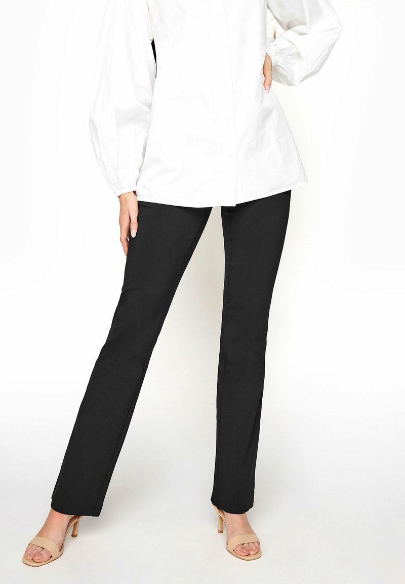 Svarta rakbenade byxor i slätt tyg, kombinerade med en vit skjorta med knappar och nudefärgade högklackade skor.