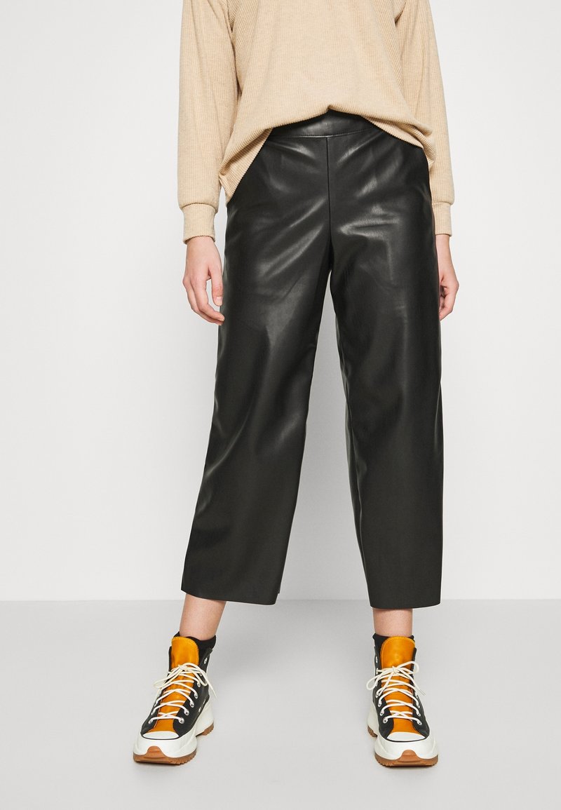 Svarta läderbyxor i cropped-stil med en slät yta och vida ben, parat med högkängor som har svarta, vita och orange detaljer.