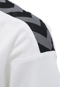 Hvid sportstrøje med en sort og hvid chevron-mønstret skulderpanel, ribbet tekstur og glat stoffinish.