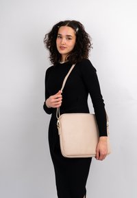Lysbeige lædertaske med en glat tekstur, rektangulær form og en aftagelig skulderrem. Har guldfarvede accenter og lynlåse.