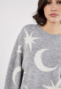 Grauer Strickpullover mit weißen Mond- und Sternmustern, Rundhalsausschnitt und einer weichen, strukturierten Oberfläche.