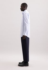 Lichtblauwe lang-sleeve shirt met een op maat gemaakte pasvorm, button-down kraag en één borstzak, gecombineerd met donkere broek en zwarte schoenen.