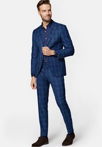 Granatowy, kraciasty garnitur o dopasowanym kroju, z dwiema guzikami w marynarce, uzupełniony ciemnoniebieską koszulą i brązowymi butami.