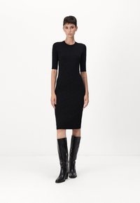 Abito nero aderente con maniche corte e un motivo testurizzato, abbinato a stivali neri alti e lucidi. Il design è lungo fino al ginocchio e aderente.