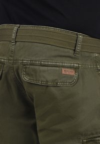 Chinos vert olive avec une ceinture élastique tissée, dotés d'une poche arrière et d'une étiquette logo cousue. Le tissu a une texture lisse.