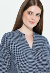 Blusa de fondo azul marino con un diseño geométrico blanco y tela liviana. Corte clásico con detalles sutiles.