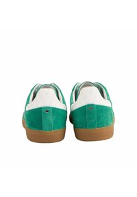 Baskets en daim vert avec des accents en cuir blanc, une semelle en caoutchouc beige et un design de talon matelassé, présentant un petit logo en métal.