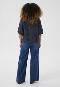 Blusa navy con motivo floreale testurizzato, maniche a sbuffo e dettagli ad occhiello; abbinata a jeans in denim blu a gamba larga e scarpe marroni.
