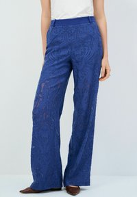 Pantalones azul celeste de encaje con una textura transparente, diseño de pierna ancha y detalles estampados. Una cinturilla elástica mejora el ajuste y la comodidad.