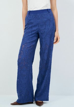 Pantaloni blu in pizzo con una texture trasparente, design a gamba larga e dettagli decorativi. Un elastico in vita migliora la vestibilità e il comfort.