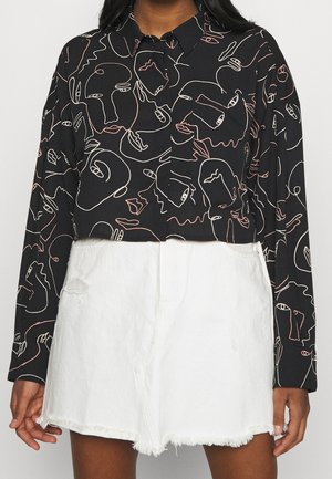 Camiseta negra de manga larga recortada con un patrón abstracto de caras en línea continua combinada con shorts de mezclilla blancos de cintura alta y dobladillo deshilachado.