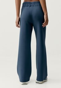 Modré, široké nohavice vyrobené z hladkej, mäkkej látky s elastickým pásom. Majú čistý dizajn bez viditeľných vzorov alebo kovania.