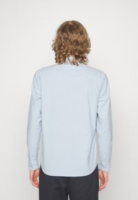 Ljusblå långärmad skjorta i mjukt tyg, med knapp-down krage, ryggstycke och rundad nederkant. Slät textur med knäppning vid ärmsluten.