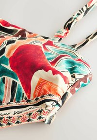 Farebný vzorovaný vrchný diel bikín s nastaviteľnými tenkými ramienkami, s abstraktnými tvarmi v červených, tyrkysových, oranžových, čiernych a krémových tónoch.