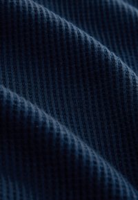 Tissu en maille gaufrée bleu foncé avec un motif texturé en grille et des plis doux créant des ombres diagonales.