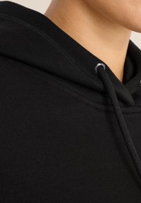 Sudadera negra con cordón. Primer plano de la textura de la tela, mostrando algodón suave y liso, con detalles de costura contrastantes.