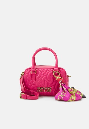 Sac à main matelassé rose vif avec deux poignées, logo doré "Versace Jeans Couture", bandoulière amovible et un foulard en soie rose à motifs attaché à une des poignées.