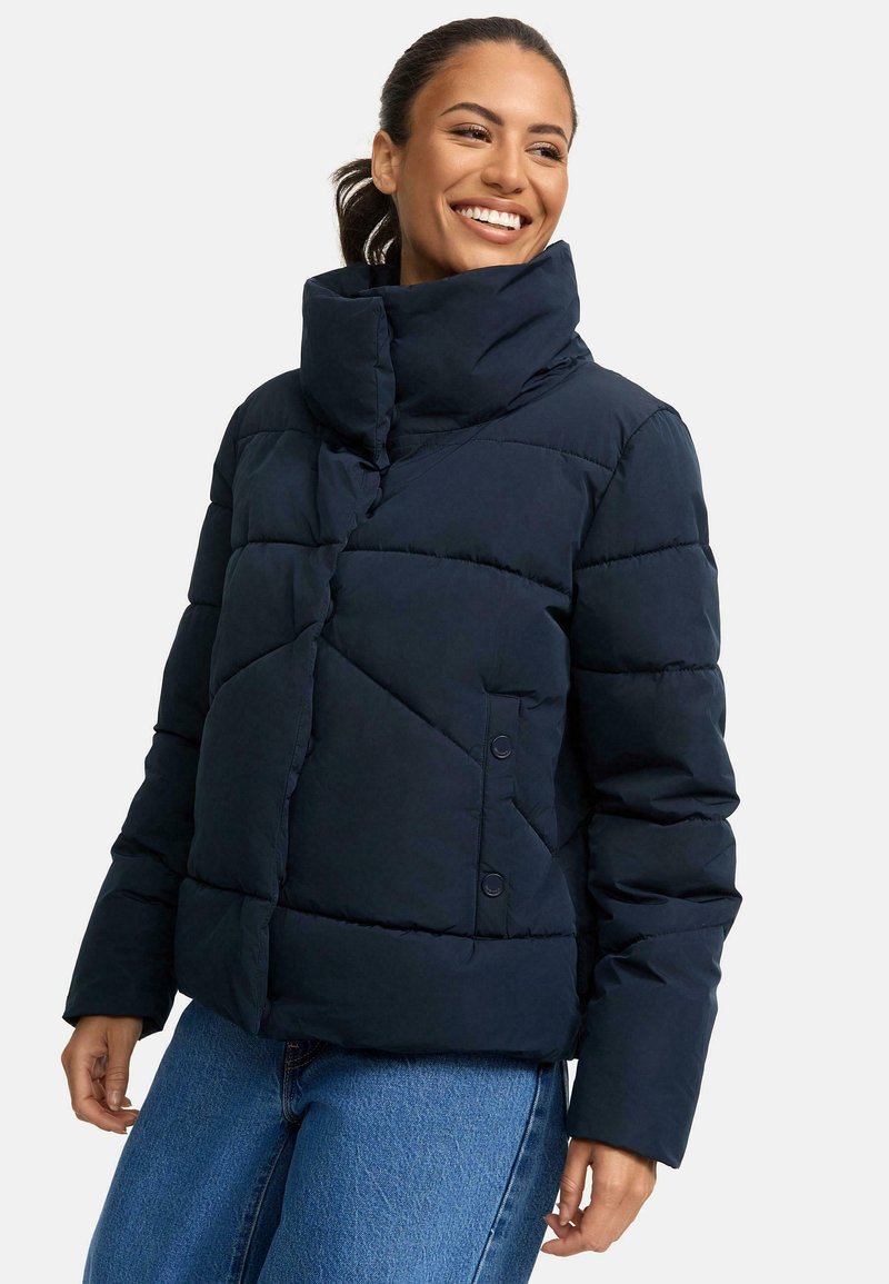 Navy puffjacka med hög krage, diagonalt quiltat mönster, knappdetaljer och en kort design, tillsammans med blå jeans.