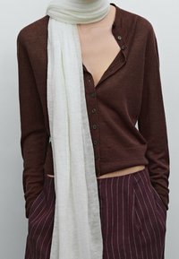 Bruin gebreid shirt met lange mouwen en knopen, met een V-hals ontwerp, gecombineerd met een witte lichte sjaal en bordeauxrode pantalon met krijtstrepen.