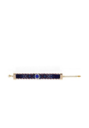 Bracelet en tissu bleu avec des bords tressés rouges et blancs, pierre précieuse bleue centrale entourée de petites pierres claires, et fermoir chaîne dorée.