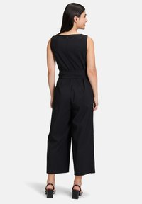 Fekete ujjatlan overál, amelynek fitted derékrésze, széles lába és hátul cipzáros záródása van. Simább szövet és öv hangsúlyozza a sziluettet.