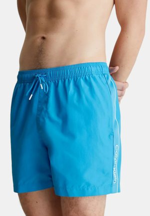 Pantaloni da nuoto blu realizzati in tessuto leggero. Presentano un elastico in vita, un cordoncino e un logo bianco lungo il lato. Texture liscia.