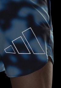 Shorts de sport bleus et noirs avec une texture lisse et un logo triangulaire blanc réfléchissant situé en bas à gauche.