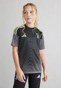 Čierny športový dres s krátkym rukávom a žltými akcentmi, s dynamickým vzorom a logom. V kombinácii s čiernymi nohavicami s logom.