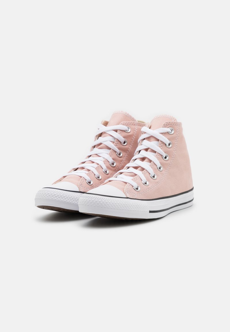 Un par de zapatillas altas de lona rosa con cordones blancos, punteras de goma y suelas blancas con rayas negras sobre un fondo blanco.