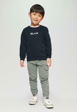 Dunkelblaues Sweatshirt mit dem Text "SLVR", hellgraue Cargo-Hosen mit Taschen und weiße Sneakers mit beigen Akzenten; stehendes Kind mit kurzen Haaren.