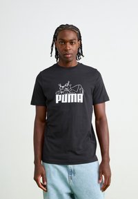 Sort bomulds t-shirt med hvid grafik af en panter og "PUMA" logoet. Runde halsudskæring, korte ærmer, afslappet pasform. Lyseblå denim shorts fremhævet.