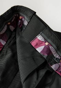 Intérieur d'un vêtement noir avec une texture lisse, présentant une doublure colorée à motifs dans des tons de violet, rouge et rose. Ceinture élastique incluse.