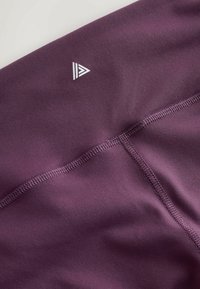 Lila sportleggings sima textúrával, háromszögletű fehér logóval és lapos varrásokkal a kényelmért.