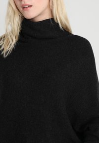 Pull noir à col roulé surdimensionné en tissu tricoté doux et texturé ; présente une silhouette décontractée et un design sans coutures.