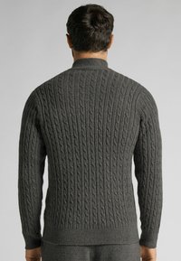 Tmavě šedý svetr s kabelkovým pletením a vysokým límcem, textura vzoru, žebrované manžety a pásek, který předvádí těsný střih a detailní zpracování.