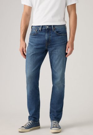 Blå denimjeans med rak benen passform, utrustade med fem fickor, metalldetalj i knäppning och lätt blekning. Matchas med blå sneakers.