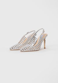 Sølv strappy høyhælte slingback-sko med spiss tå og tynne stiletthæler på en enkel hvit bakgrunn.