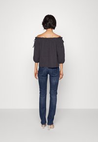Off-shoulder, mörkgrå blus med knutna ärmar, i kombination med medelhöga blå jeans. Slätt tyg med avslappnad passform. Genomskinliga skor.