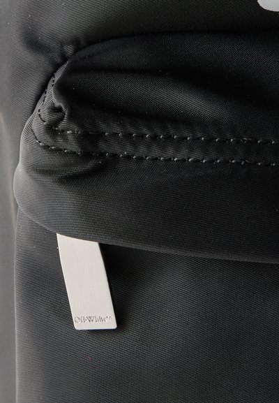Κοντινό πλάνο σε μαύρη υφασμάτινη τσέπη με φερμουάρ και ασημί τράβηγμα φερμουάρ με το λογότυπο Off-White.