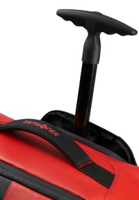 Red duffel bag with black accents featuring a retractable handle, padded strap, and zippered opening for easy access.