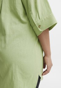 Heled roheline, lühikeste varrukatega shirts, millel on tekstuuriga kude. Omab rullitud varrukaotsi, mis on kinnitatud väikeste nuppudega, ja külgsuundi liikumise mugavuse tagamiseks.