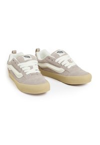Zapatillas de gamuza gris claro con acentos en blanco, suela de goma texturizada, cordones y un parche con el logo en la lengüeta. Silueta clásica de zapatilla de skate.