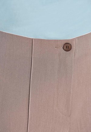 Lichtblauwe top gedragen over beige broek, met een voorzak, een bruine knoopsluiting en een gladde textuur met subtiele stiksels.