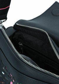 Sac à main en cuir noir avec fermeture éclair en métal argenté, doté d'une poche intérieure. Les détails incluent des découpes florales colorées sur l'extérieur.